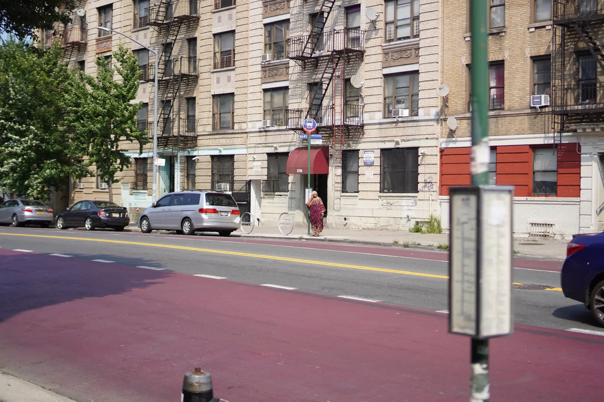 A person waits in the sun for the bus on Webster Avenue